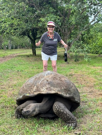 Gael Gallagher smiling next to a giant Galápagos tortoise in a lush green landscape, capturing her love for wildlife and exploration.