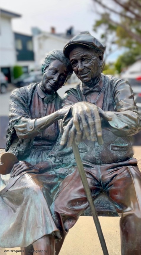 A bronze statue of an elderly couple sitting closely on a bench, symbolizing timeless love and companionship, located in Carmel.
