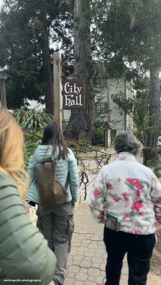 Visitors walk past the charming Carmel-by-the-Sea City Hall, surrounded by lush greenery and historic architecture, during a guided tour with Gael Gallagher.