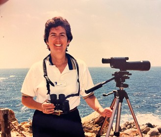 Gael, an experienced naturalist guide, stands by the ocean at Point Lobos with a telescope and binoculars, ready to lead an outdoor tour exploring California’s coastal wildlife and scenic landscapes.