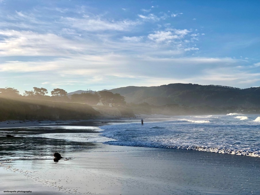 A tranquil scene at Carmel Beach with gentle waves, soft evening light, and coastal bluffs in the distance.